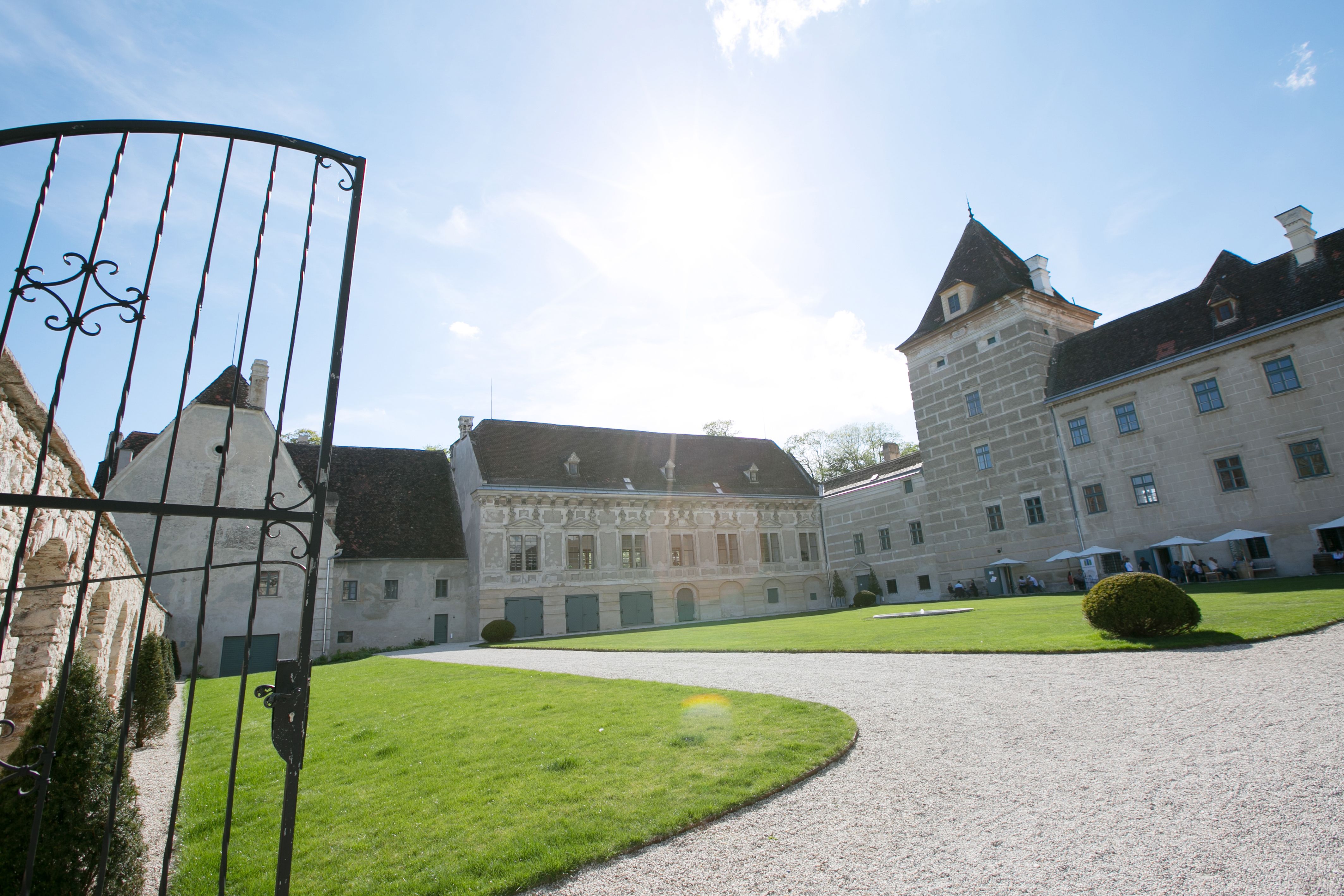 A walpersdorfi kastély bejárata nyitott kapuval, pázsit és történelmi épület a háttérben.