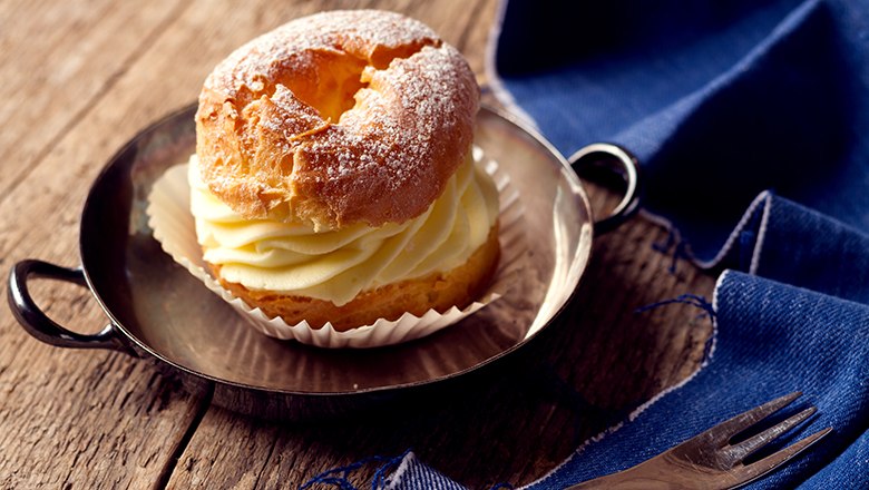 A filled choux pastry ring in a small pan, next to it a blue cloth and a fork., &copy; Sooo gut schmeckt die Bucklige Welt/ Viktoria Kornfeld