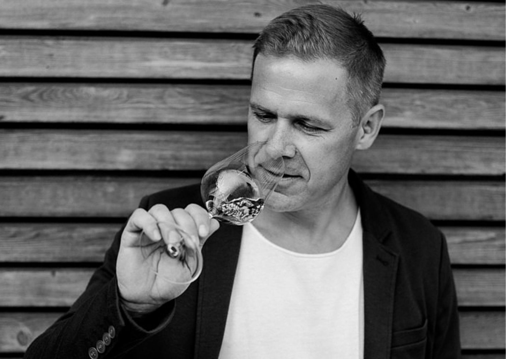 Egy férfi egy fából készült fal előtt egy pohár bort szagolgat.