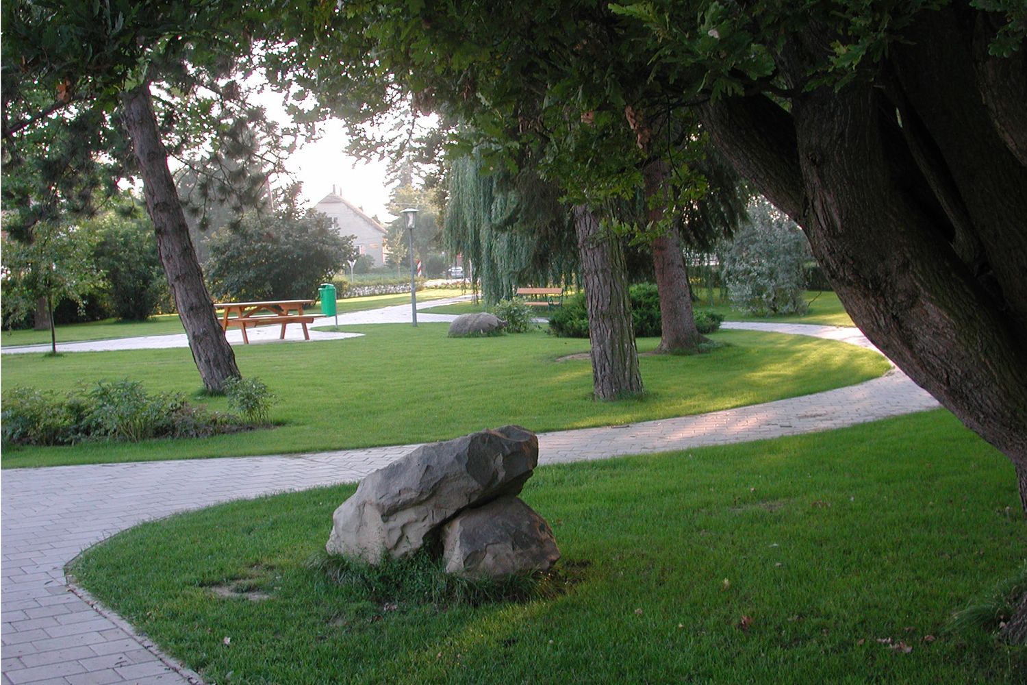 Gondozott park fákkal, ösvényekkel és padokkal.