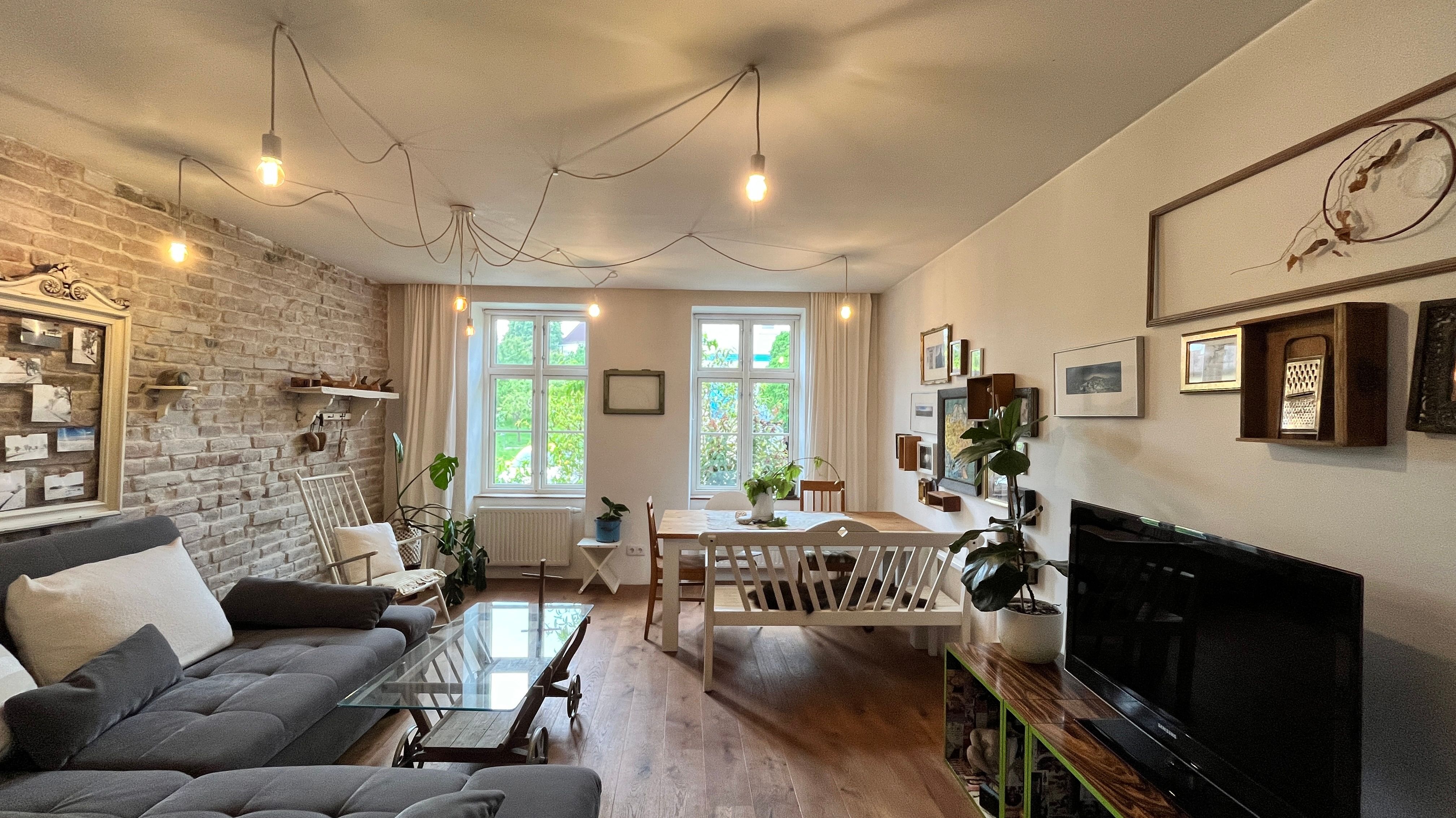 Hangulatos nappali szürke kanapéval, fa asztallal, növényekkel és fali dekorációval.