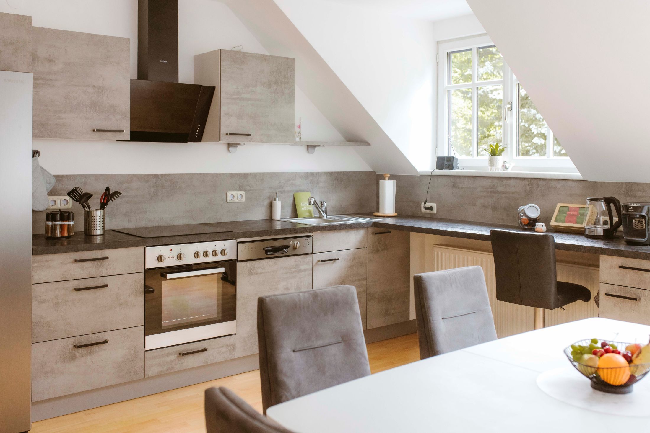 Modern konyha szürke szekrényekkel, étkezőasztallal és gyümölcstállal.