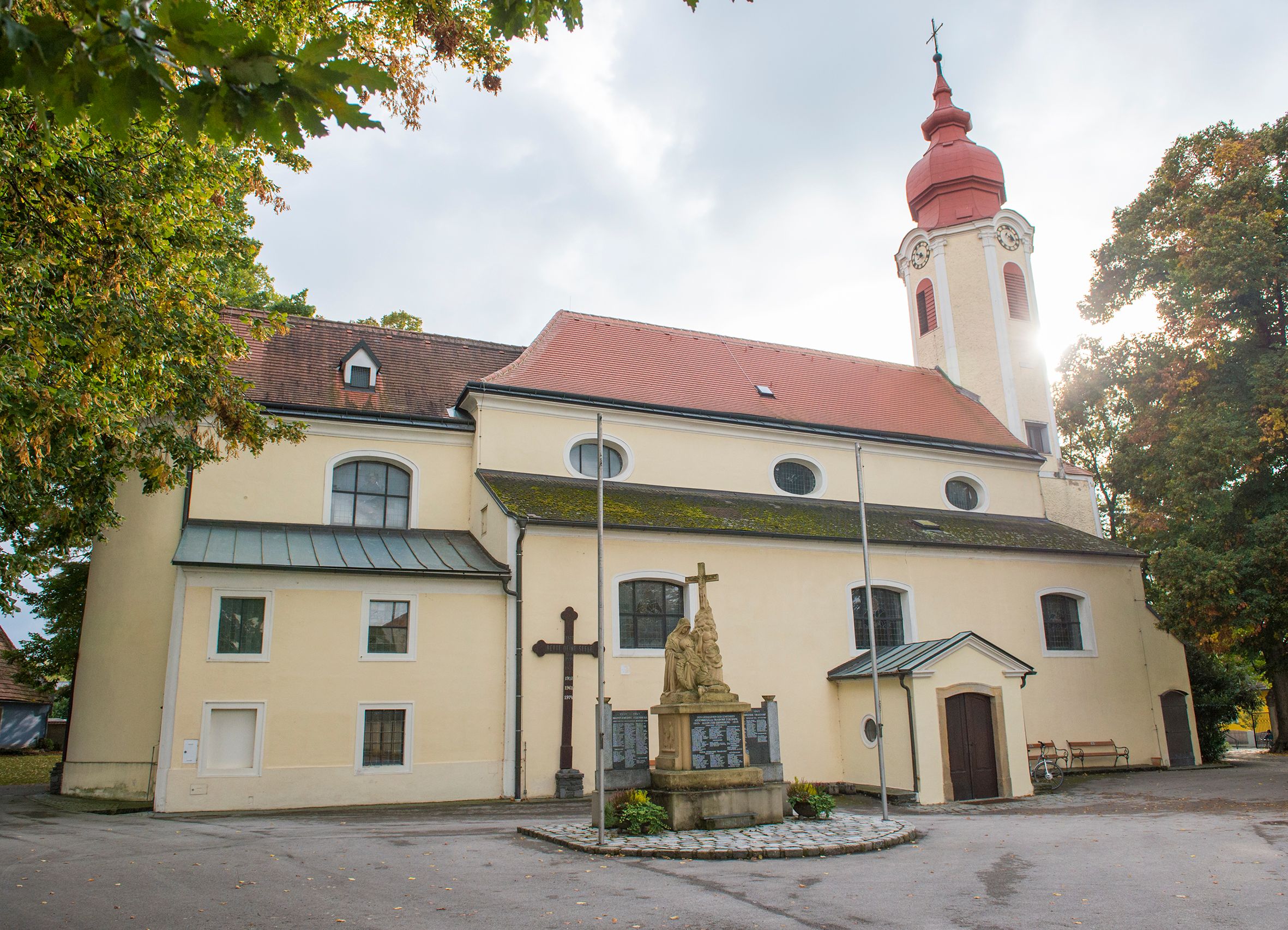 Heiligeneich plébániatemplom, előtérben szobor és kereszt.