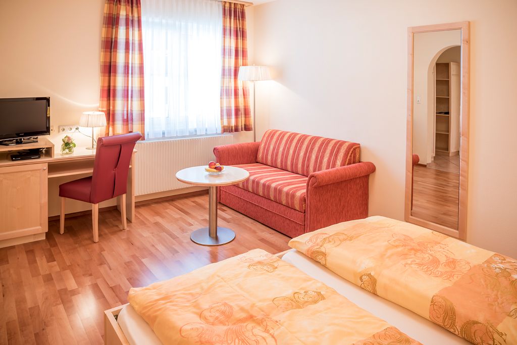 Hangulatos vendégszoba franciaággyal, piros kanapéval, íróasztallal, TV-vel és nagy tükörrel.