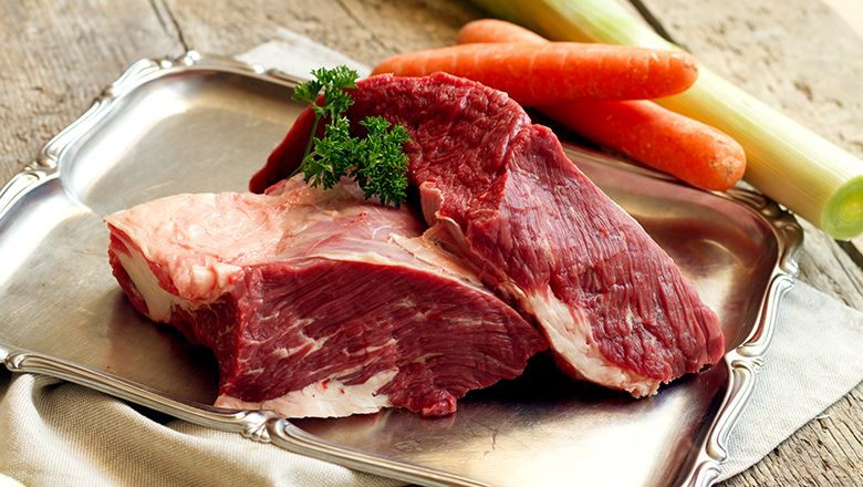 Két darab nyers hús egy ezüsttálcán egy faasztalon. Mellette sárgarépa és póréhagyma.