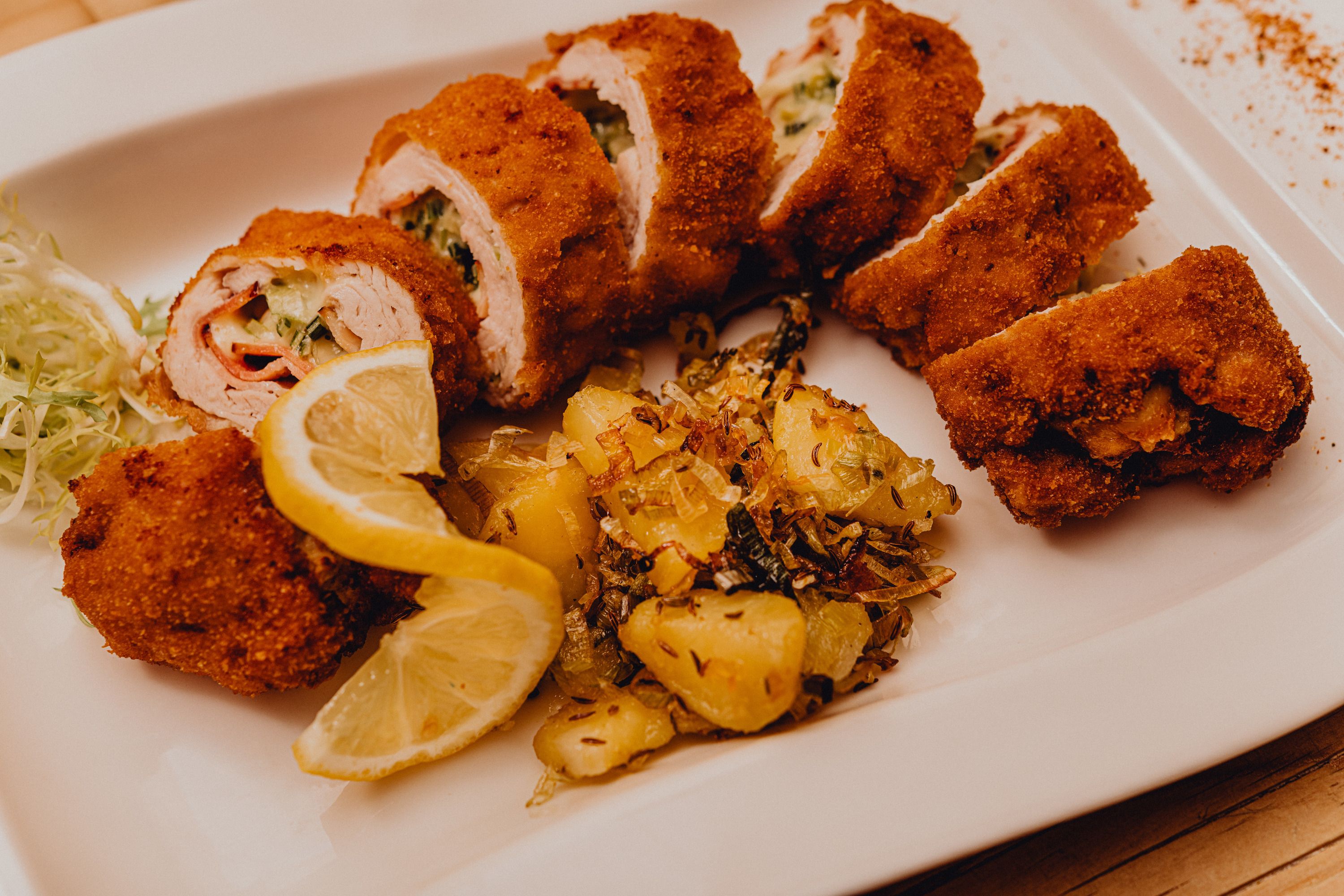 Töltött, sült pulykafilé burgonya körettel és citromszeletekkel fehér tányéron.