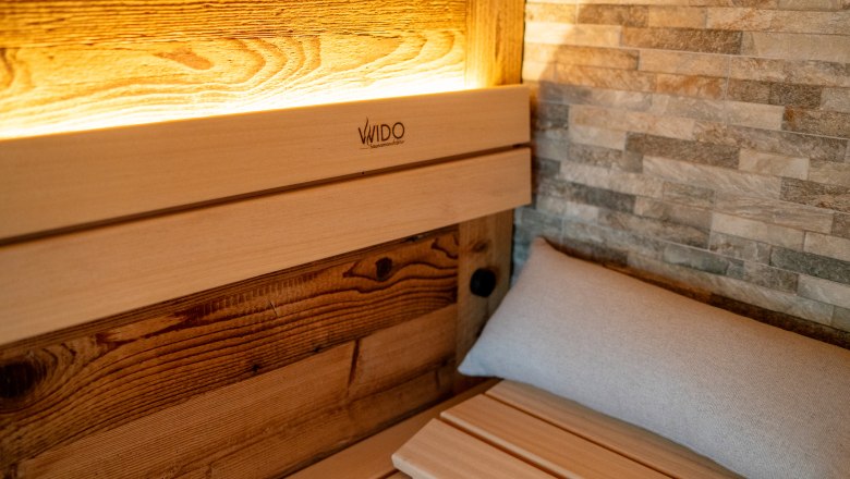 Belső nézet egy szaunáról, faburkolattal és kőfallal.