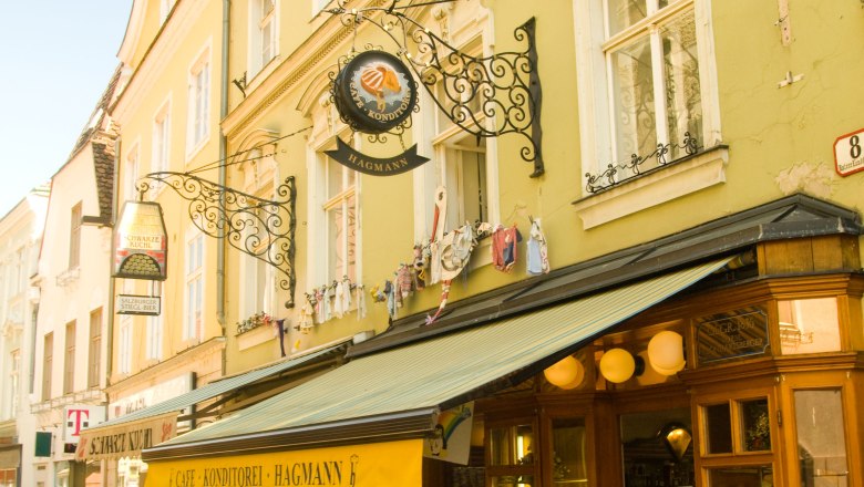 A Konditorei Hagmann k&uuml;lső n&eacute;zete s&aacute;rga előtetővel &eacute;s utcai k&aacute;v&eacute;z&oacute;val.