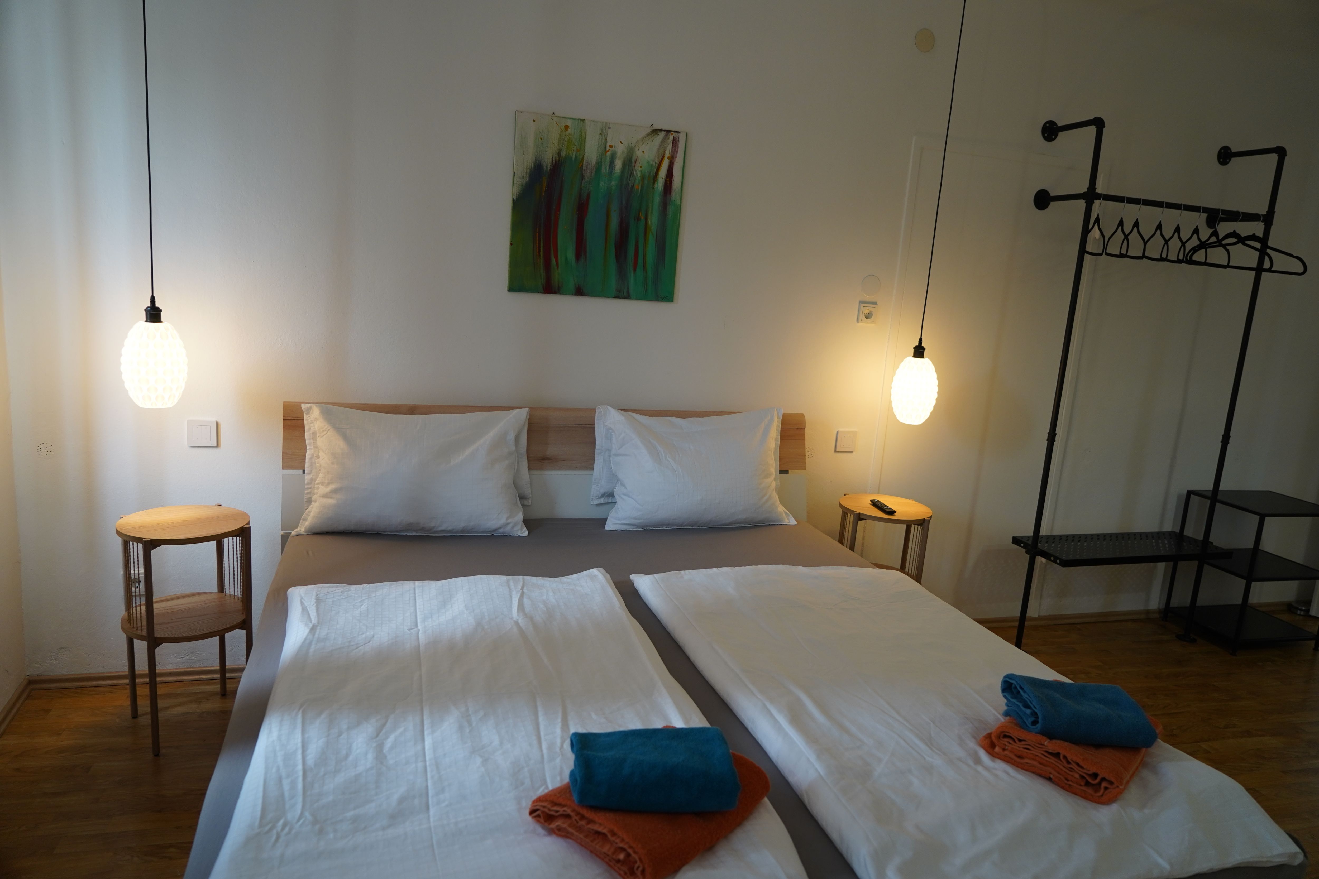 Modern hálószoba franciaággyal, két éjjeliszekrénnyel, függőlámpákkal és törölközőkkel az ágyon.