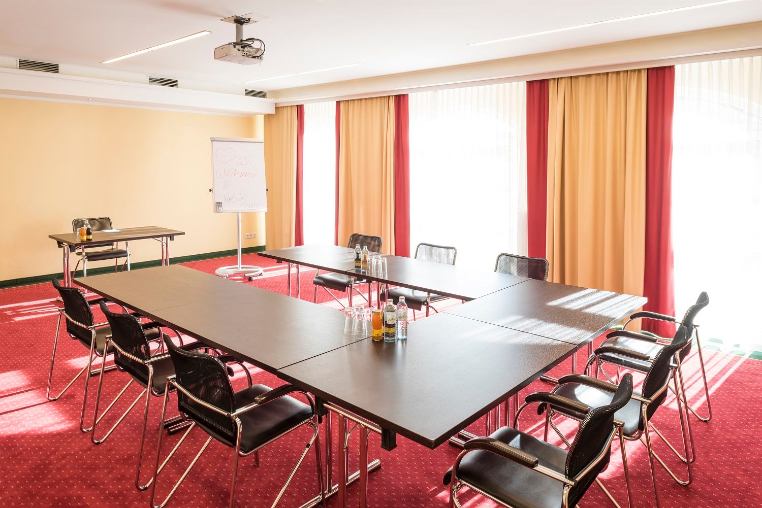 Konferenciaterem U alakú asztallal, székekkel, flipcharttal és projektorral.