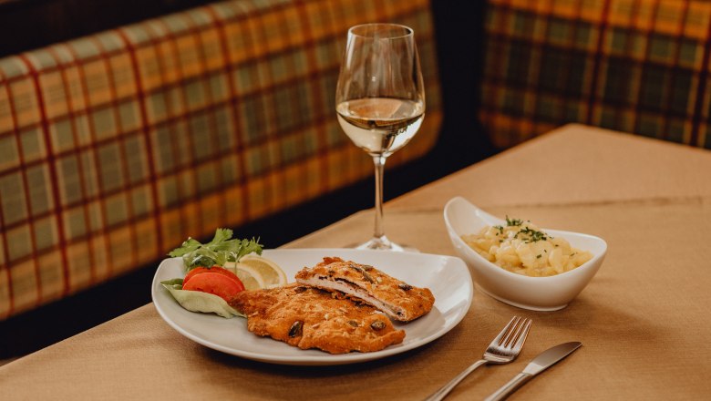 Egy tányér cordon bleu, saláta körettel és egy pohár fehérborral az asztalon.