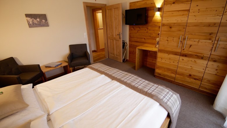 Hálószoba franciaággyal, fabútorokkal és TV-vel a falon.