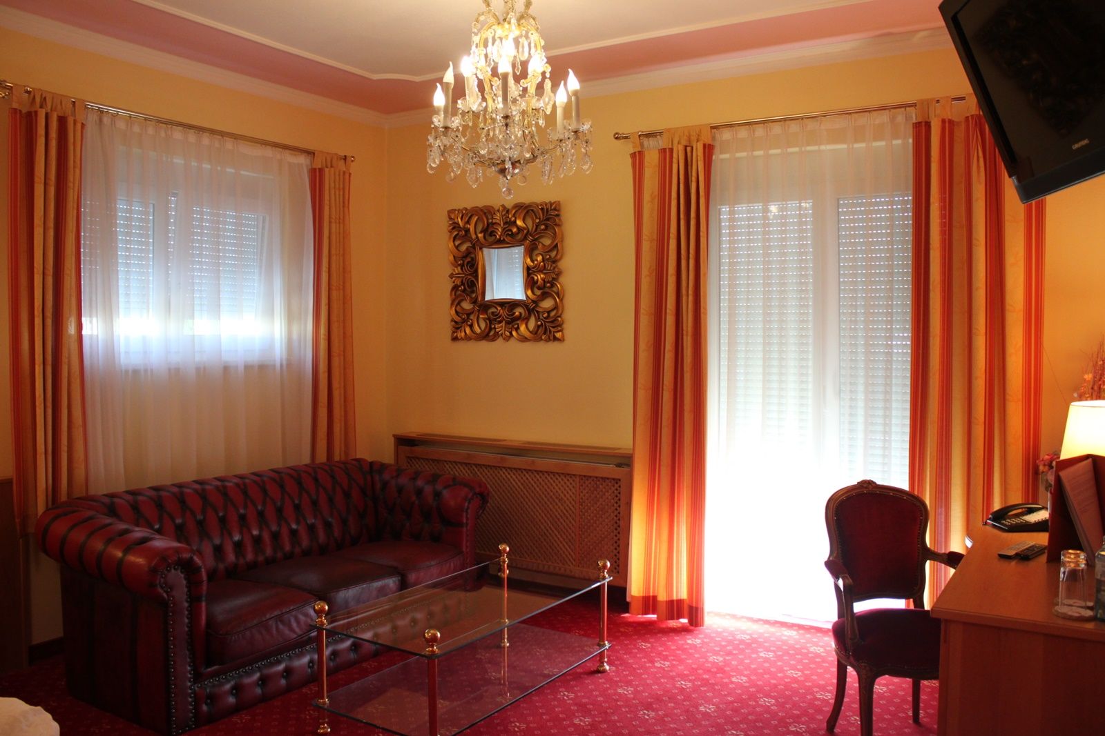 Elegáns nappali bőrkanapéval, üvegasztallal, csillárral és piros függönyökkel.