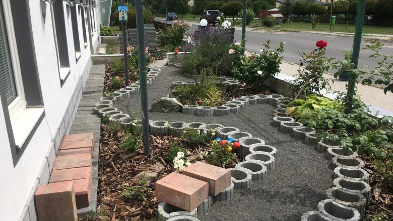 Egy kis kert r&oacute;zs&aacute;kkal &eacute;s egy betont&ouml;mb&ouml;kből k&eacute;sz&uuml;lt &iacute;ves &ouml;sv&eacute;ny egy &eacute;p&uuml;let mellett.