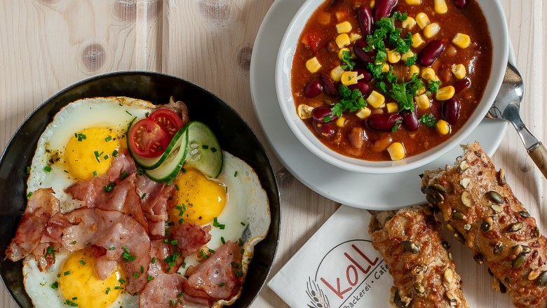 K&uuml;l&ouml;nb&ouml;ző meleg harapnival&oacute;k egy asztalon, t&ouml;bbek k&ouml;z&ouml;tt t&uuml;k&ouml;rtoj&aacute;s szalonn&aacute;val, szendvicsek &eacute;s egy t&aacute;l chili.