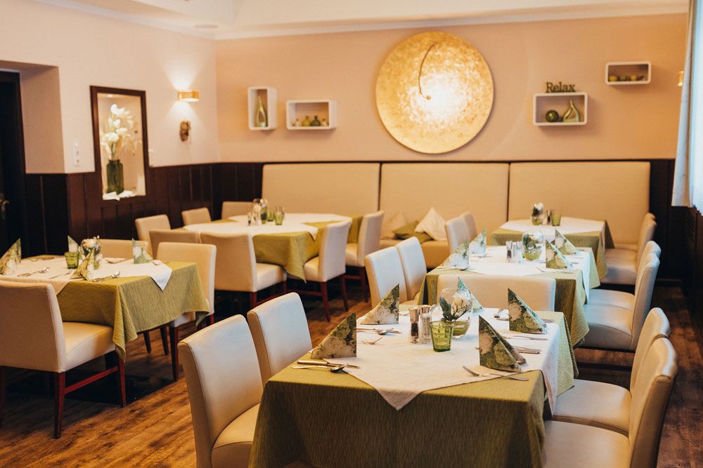 Elegáns étterem terített asztalokkal és zöld abrosszal.