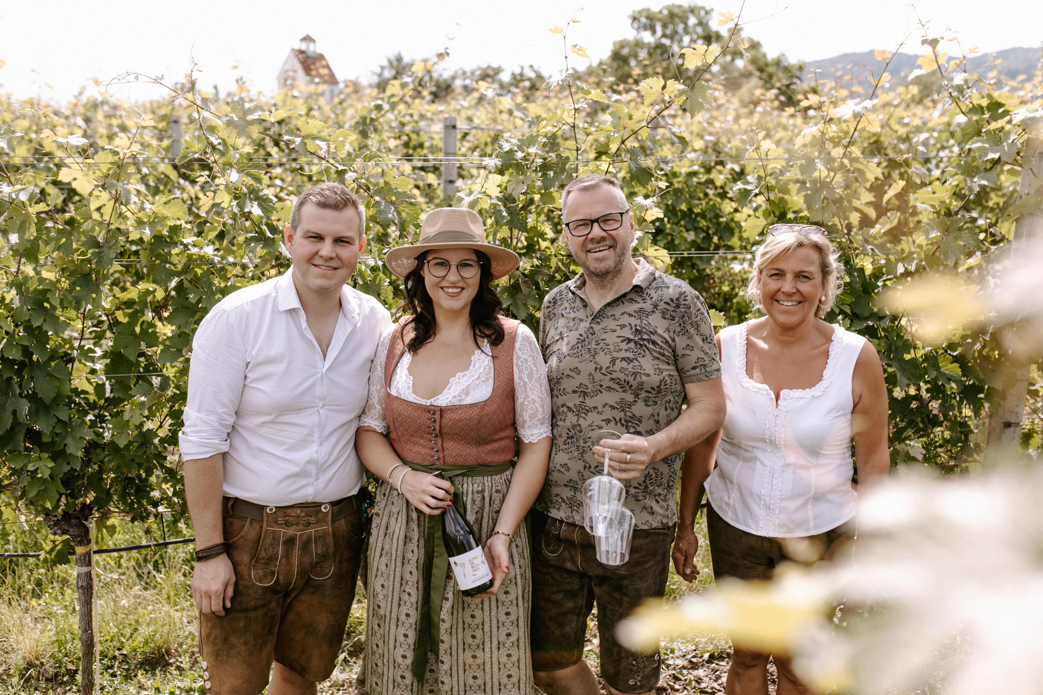 Inmitten der sanften Hügel des Wienerwaldes strahlt die Sonne auf die fruchtbaren Weinreben. Eine Gruppe von Freunden genießt die entspannte Atmosphäre und hält eine Flasche köstlichen Wein in der Hand, während sie die malerische Landschaft bewundern. Hier wird der Sommer in vollen Zügen gefeiert.