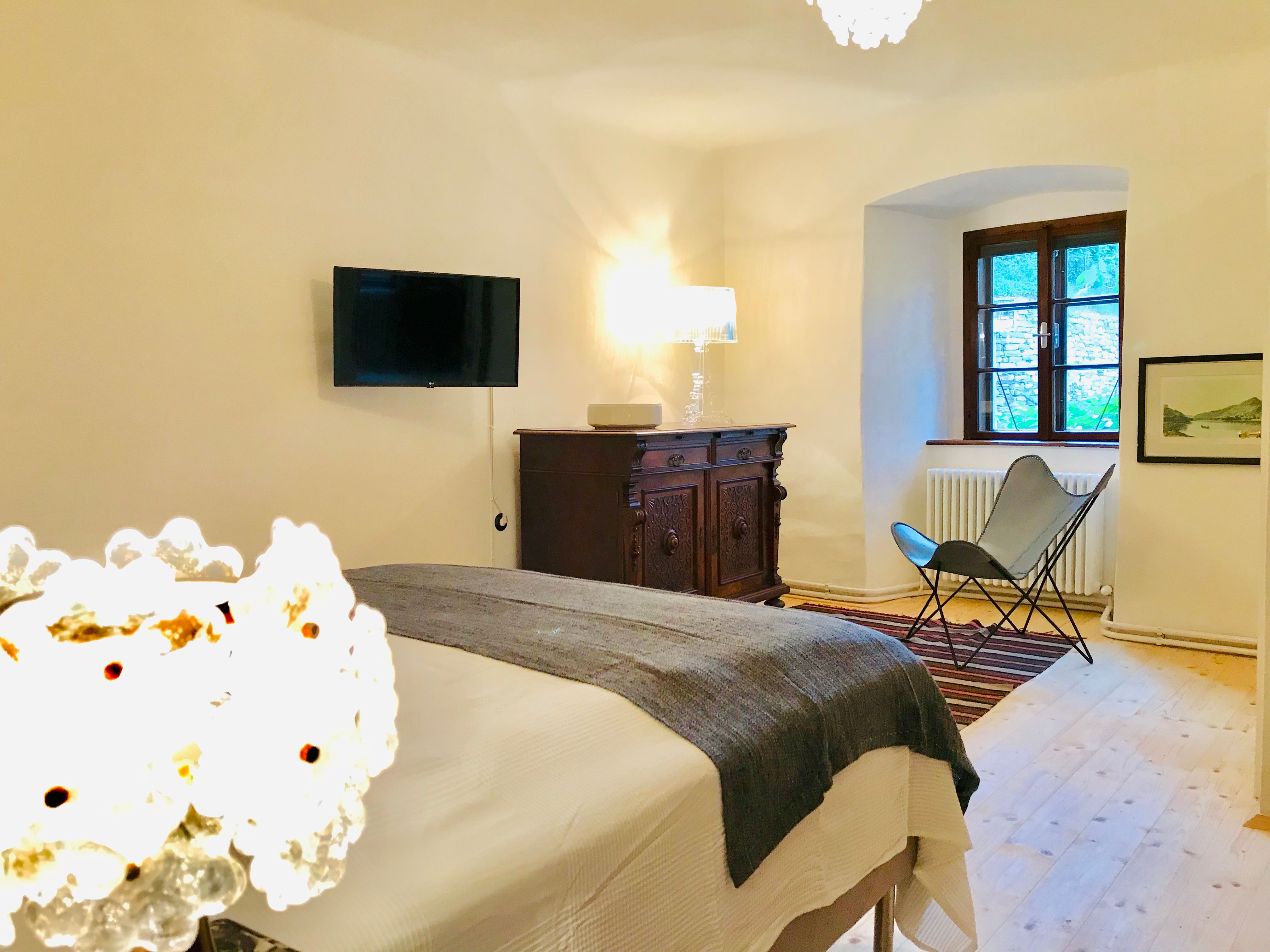 Hangulatos hálószoba ággyal, antik komóddal, karosszékkel és fali TV-vel.