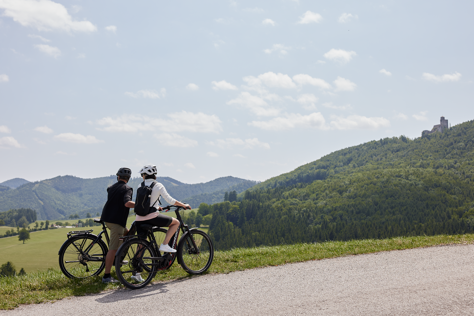 Die sanften Hügel und die üppige grüne Landschaft laden zu einer erholsamen Radtour ein. Ein Paar genießt die frische Bergluft und den atemberaubenden Ausblick auf die umliegenden Wälder und Berge. Hier, wo die Natur in voller Pracht erblüht, wird jeder Moment zum unvergesslichen Erlebnis.