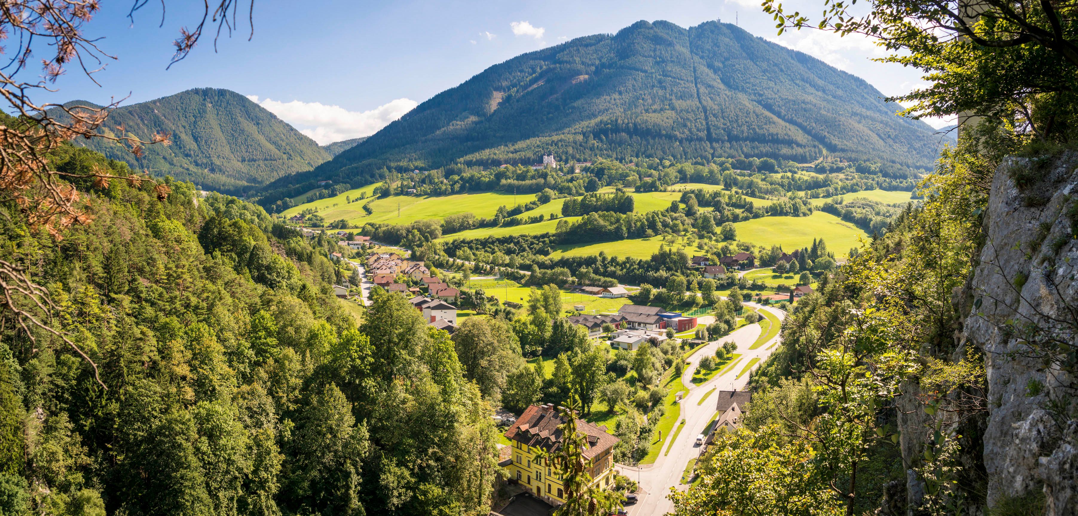 Panorámakép egy zöld völgyről, a háttérben hegyekkel, előtérben egy faluval.