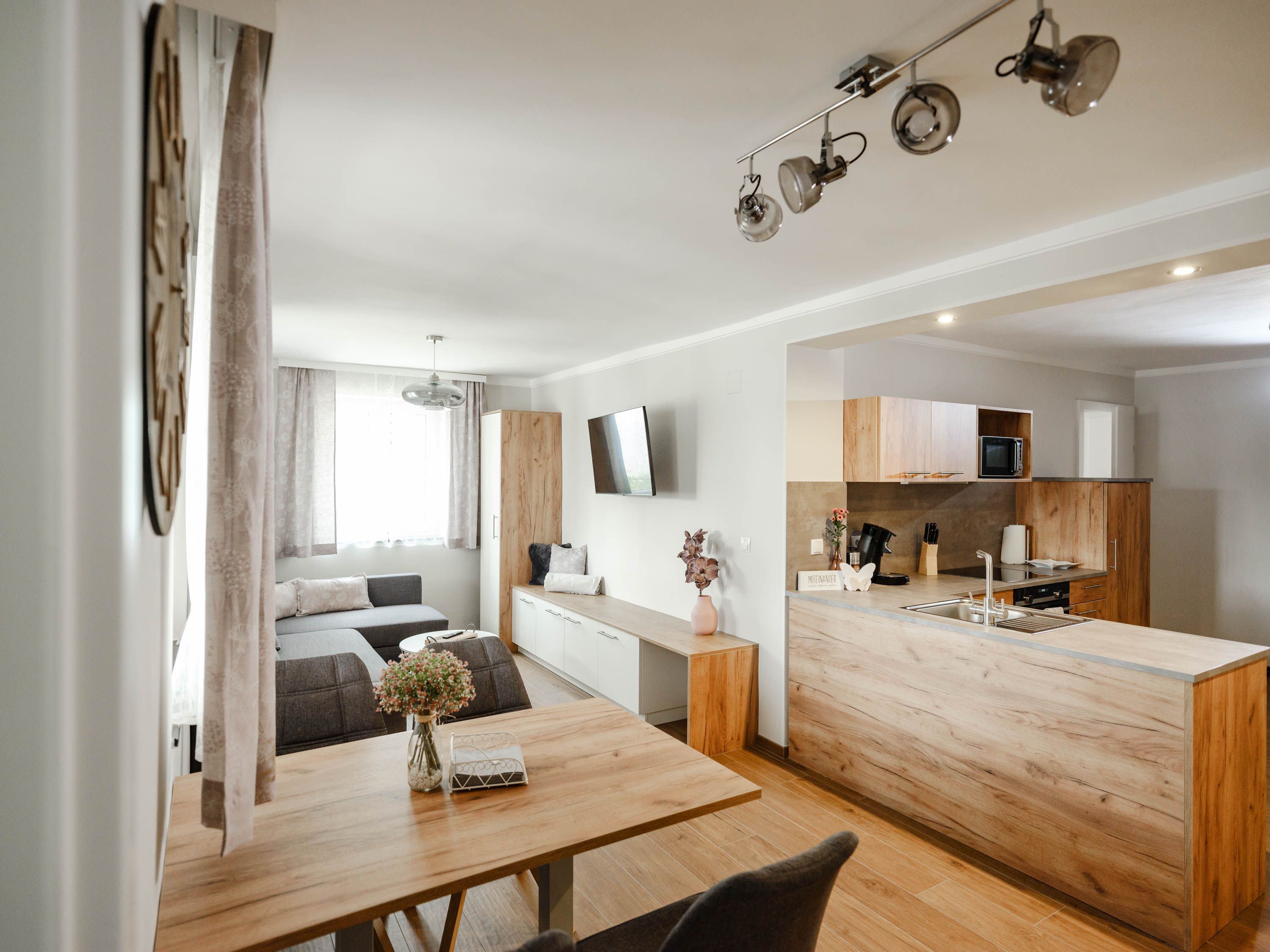 Modern étkezős konyha, fabútorokkal és szürke kanapéval.