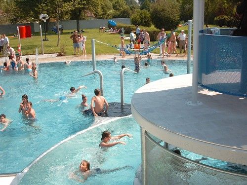 Az emberek úsznak és játszanak a csúszdával és zöld területtel ellátott szabadtéri medencében.