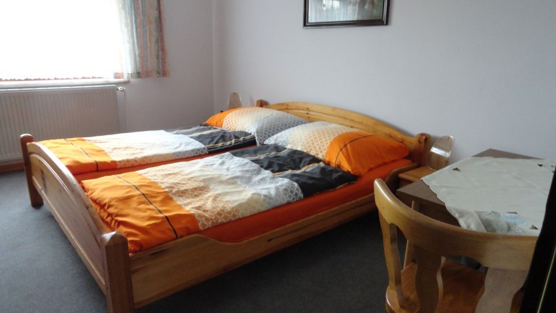 Egyszerűen berendezett h&aacute;l&oacute;szoba k&eacute;t egyszem&eacute;lyes &aacute;ggyal, asztallal &eacute;s sz&eacute;kkel.