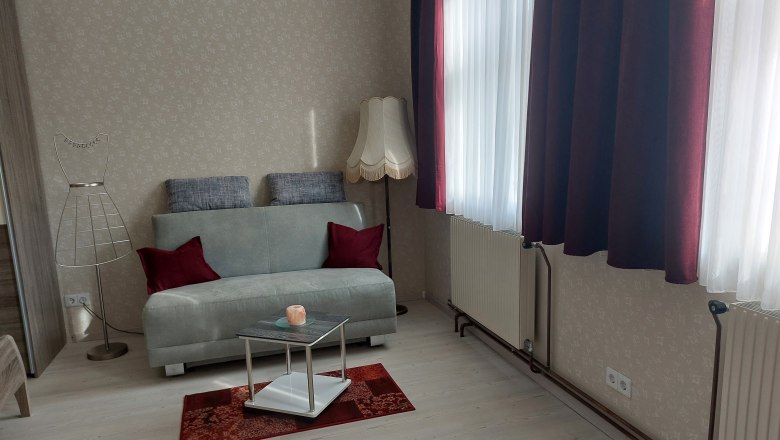 Nappali sz&uuml;rke kanap&eacute;val, piros p&aacute;rn&aacute;kkal, &aacute;ll&oacute;l&aacute;mp&aacute;val &eacute;s kis asztallal a piros szőnyegen.