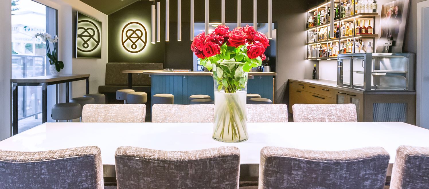 Belső nézet egy modern étteremről, fa asztalokkal és polcokkal; meleg világítás és hangulatos légkör az élvezetekhez és a kóstoláshoz.