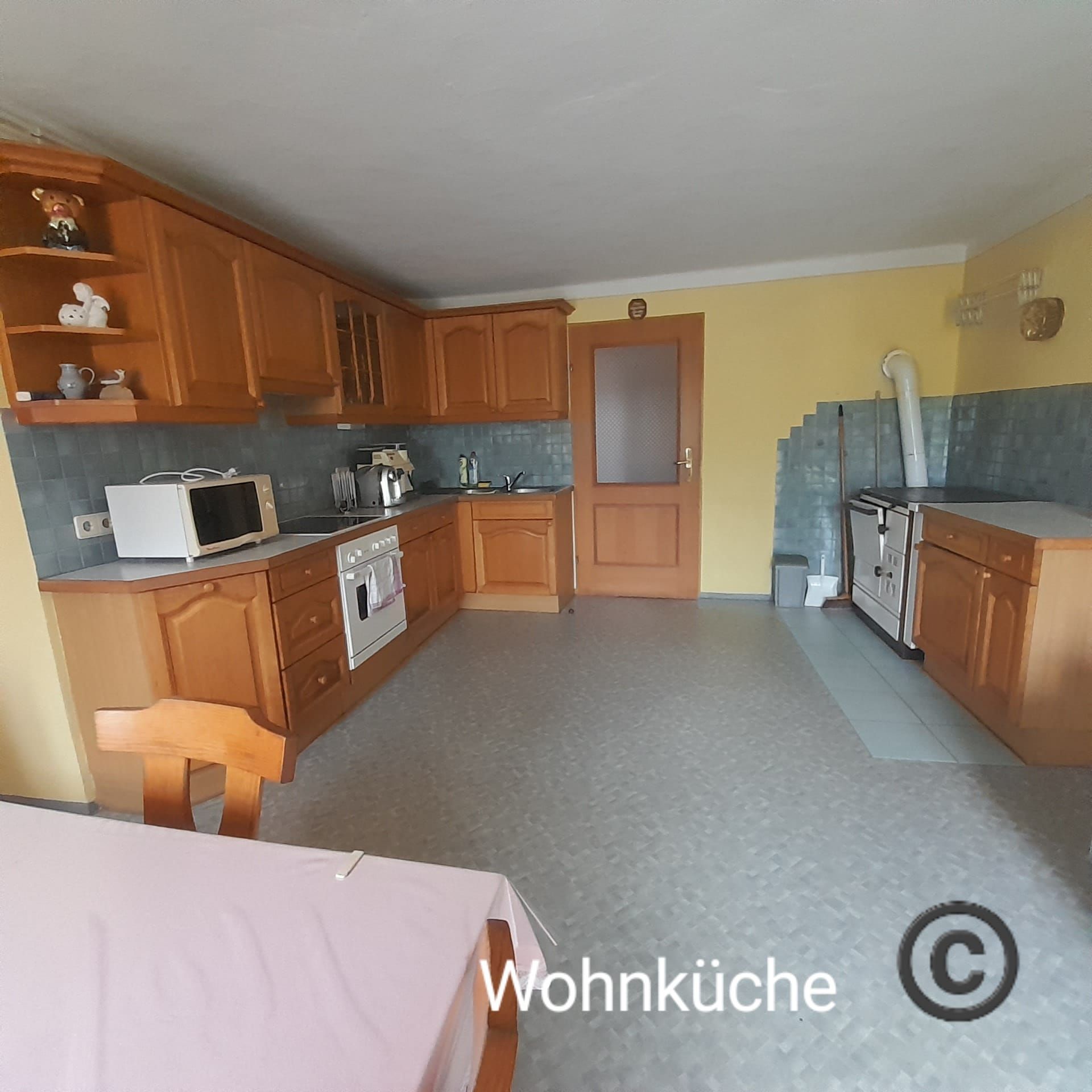 Tágas étkezős konyha fabútorokkal, étkezőasztallal, tűzhely, mikrohullámú sütő és sárga falakkal.