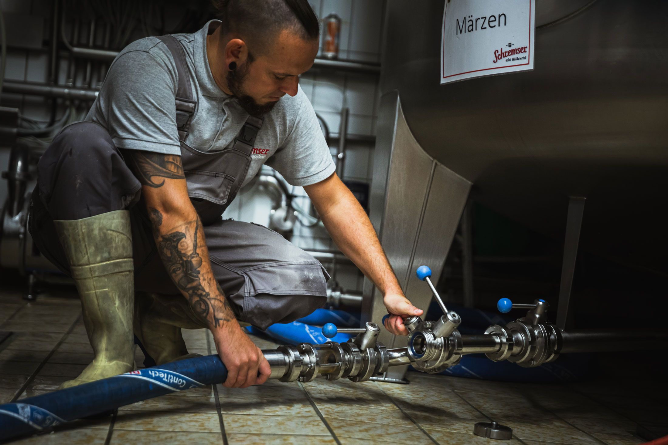 Egy munkaruhás férfi söröspoharat tart egy sörfőzde előtt.