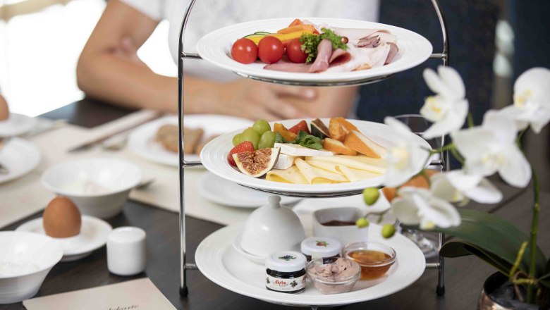 Egy reggelizőasztal, tele sajtokkal, felv&aacute;gottakkal, gy&uuml;m&ouml;lcs&ouml;kkel &eacute;s kenőcs&ouml;kkel. Az előt&eacute;rben feh&eacute;r orchidea.