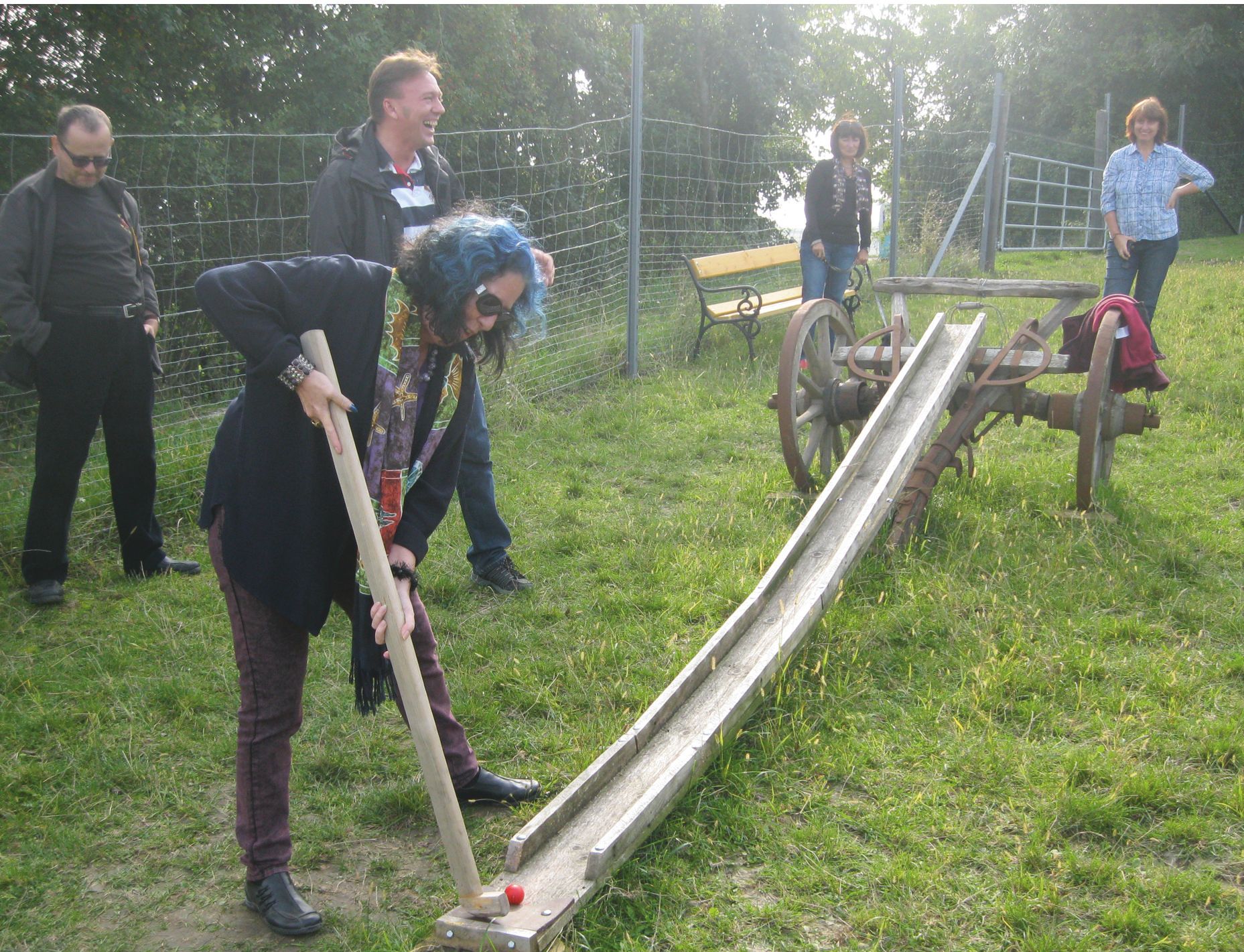 Egy személy egy faütővel farmergolfot játszik egy réten.