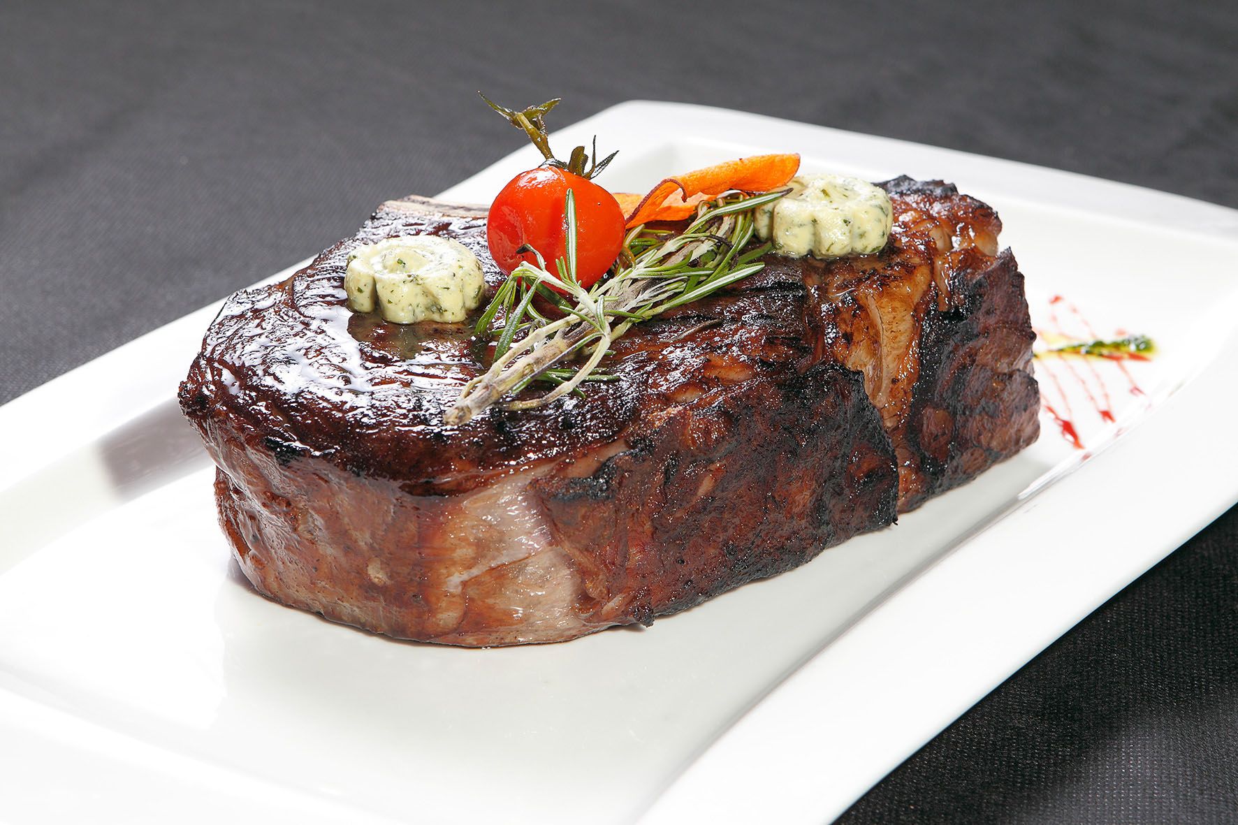 Szaftos steak fűszervajjal, rozmaringgal és cseresznyeparadicsommal fehér tányéron.