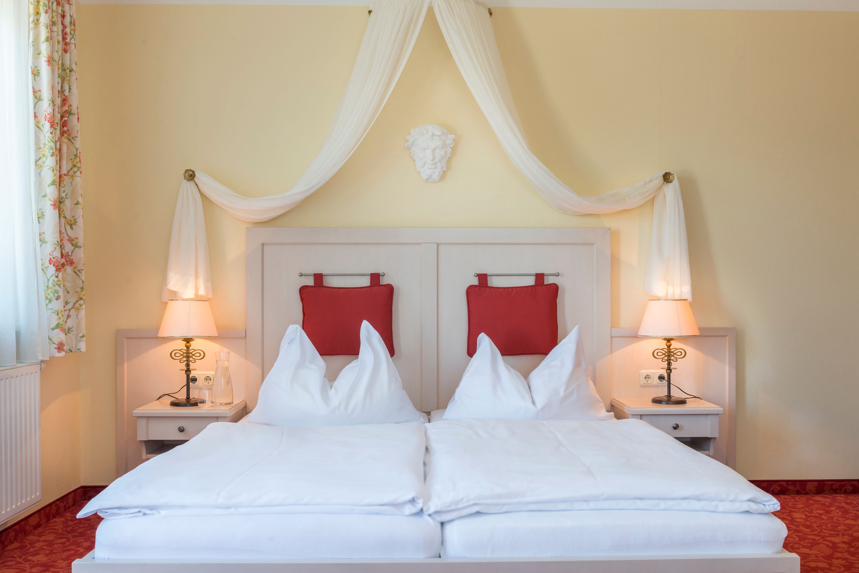 Szoba nézet a szobából, melynek tetején egy ágy van, piros kárpitozással