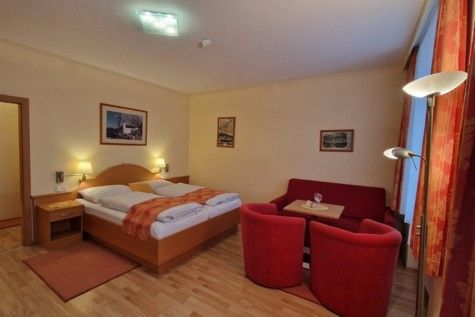 Hotelszoba franciaággyal, piros kanapéval és fotelekkel, fapadlóval és falfestményekkel.