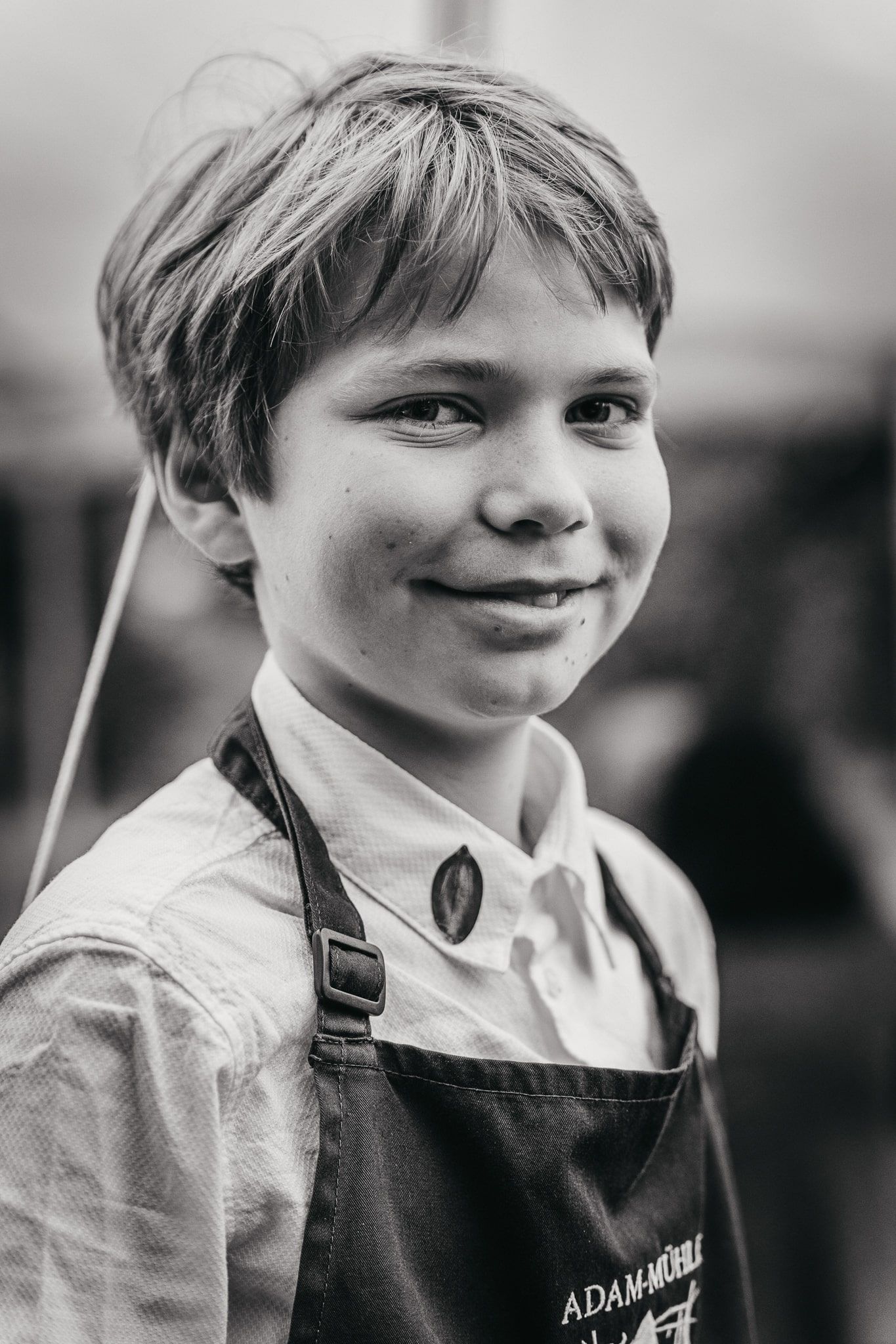 Egy "Adam-Mühle" feliratú kötényes fiú mosolyog a kamerába.