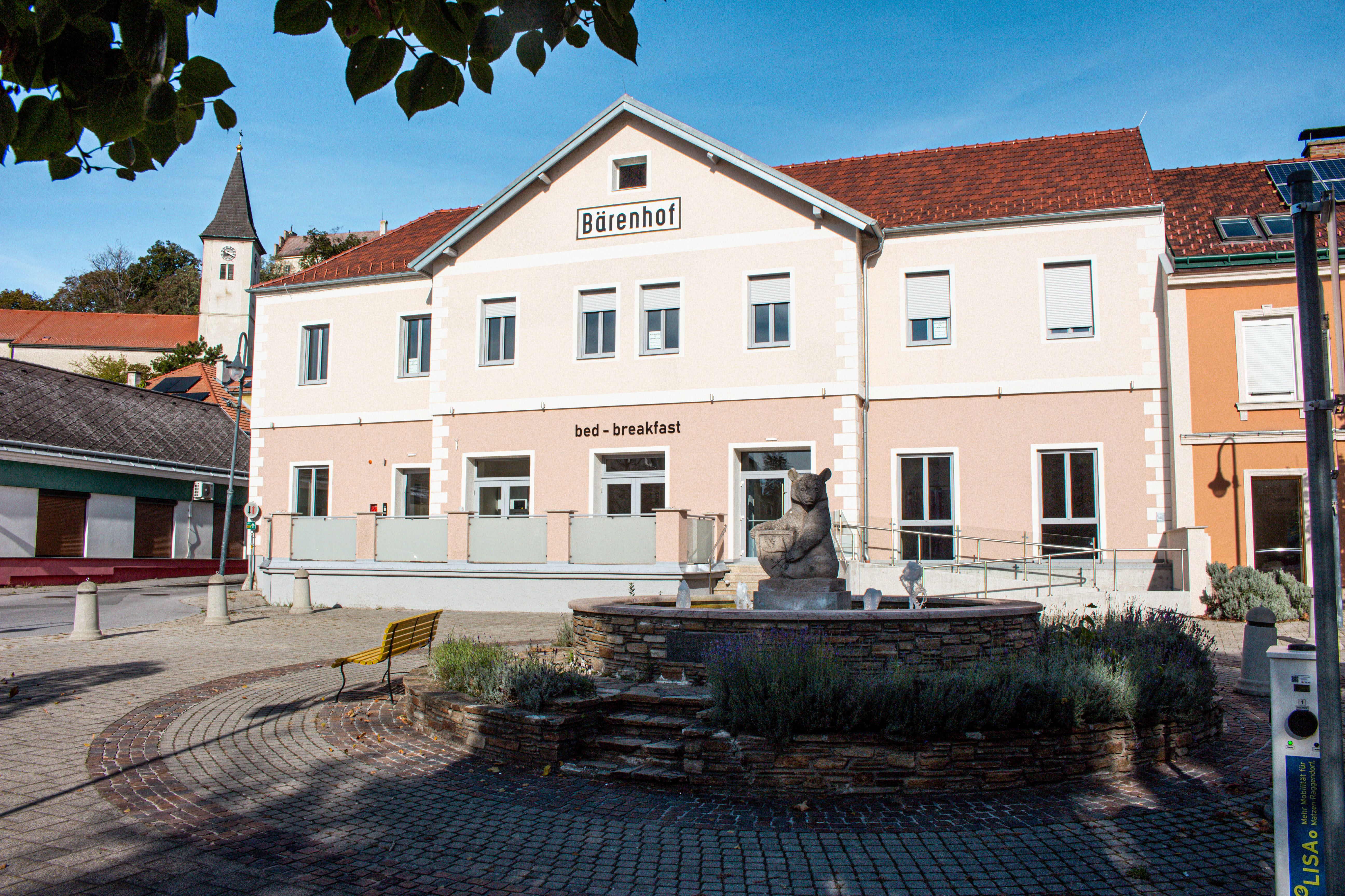A "Bärenhof" és a "bed - breakfast" feliratú épület napos környezetben, előtérben szökőkúttal.