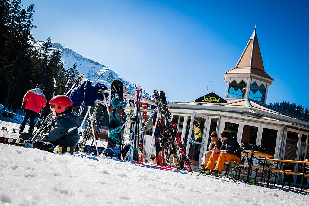 Síelők a JoSchi bár előtt sílécekkel és snowboardokkal a hóban.