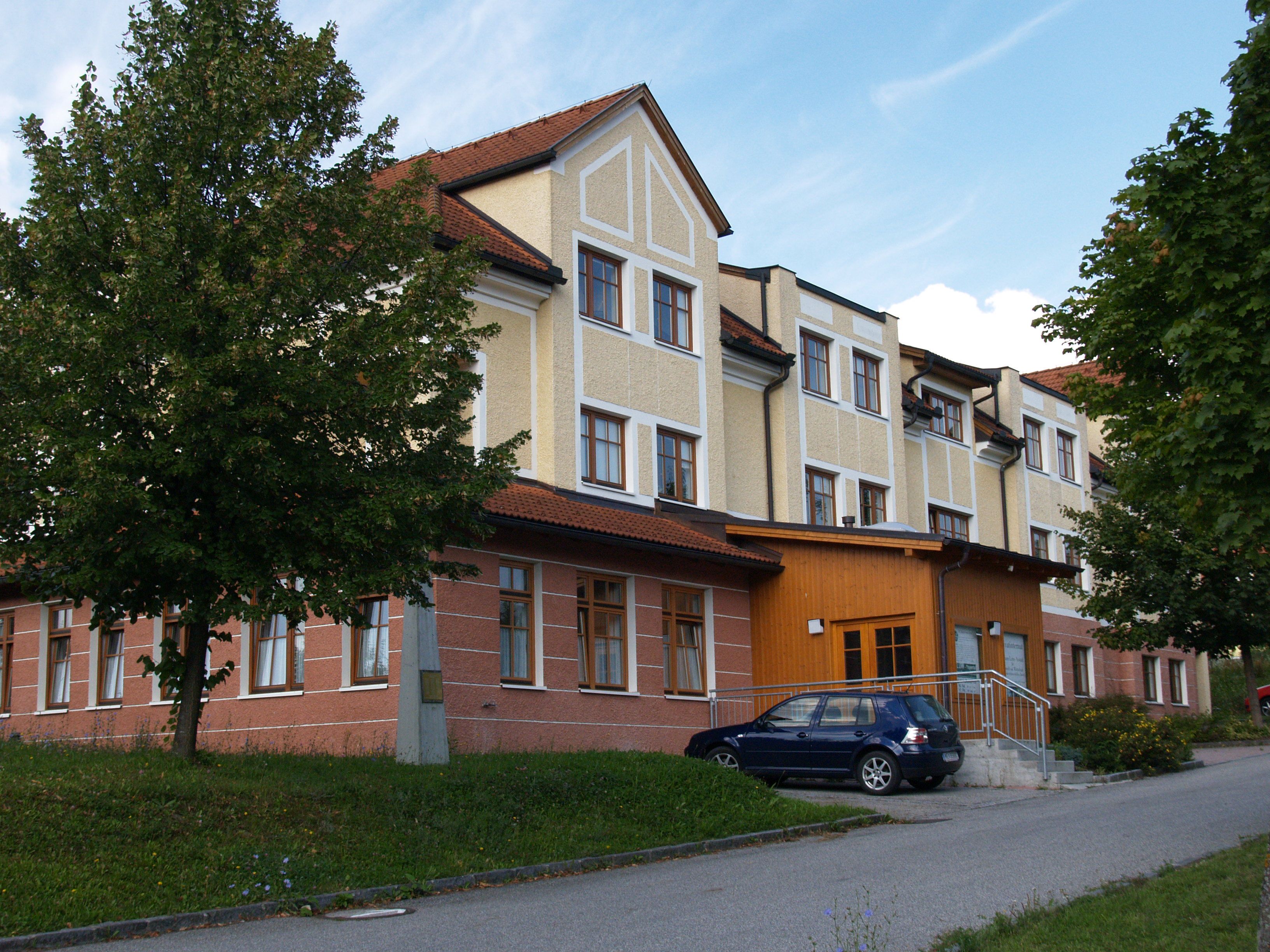 A HLUW-Yspertal vendégháza parkoló autóval és fákkal.