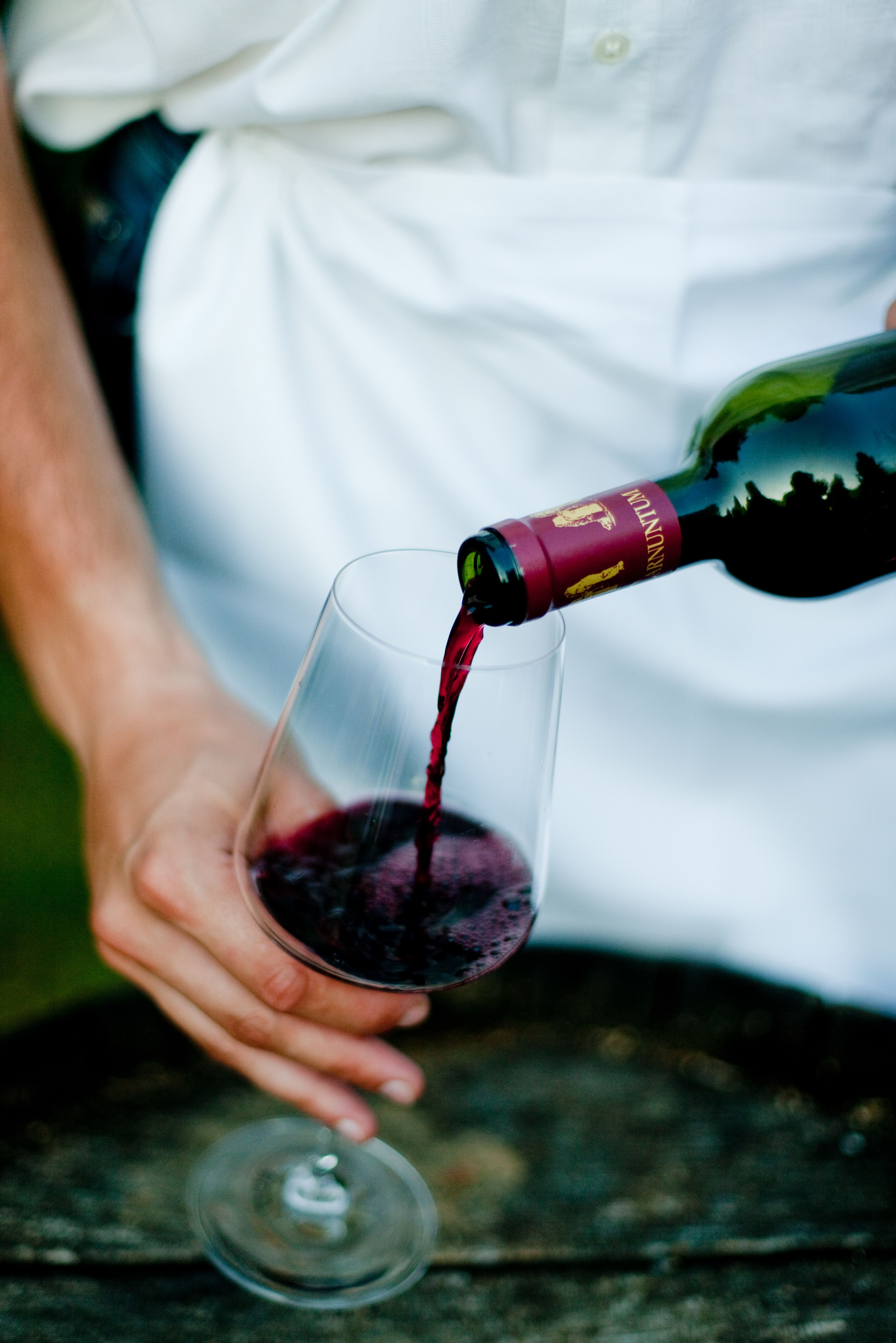 Ein elegantes Weinglas füllt sich mit tiefrotem Wein, während die sanften Hügel der Weinregion im Hintergrund erstrahlen. Der Duft von reifen Trauben und die Vorfreude auf den Weinherbst verleihen der Szene eine einladende Atmosphäre.