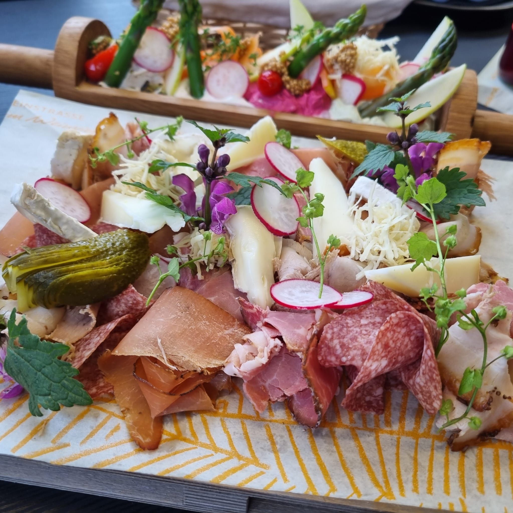 Heurigen tál különböző kolbász- és sajtfajtákkal, retekkel, uborkákkal és fűszernövényekkel, fadeszkán tálalva.