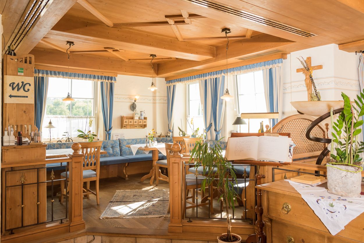 Hangulatos éttermi rész fából készült bútorokkal és kék függönyökkel.