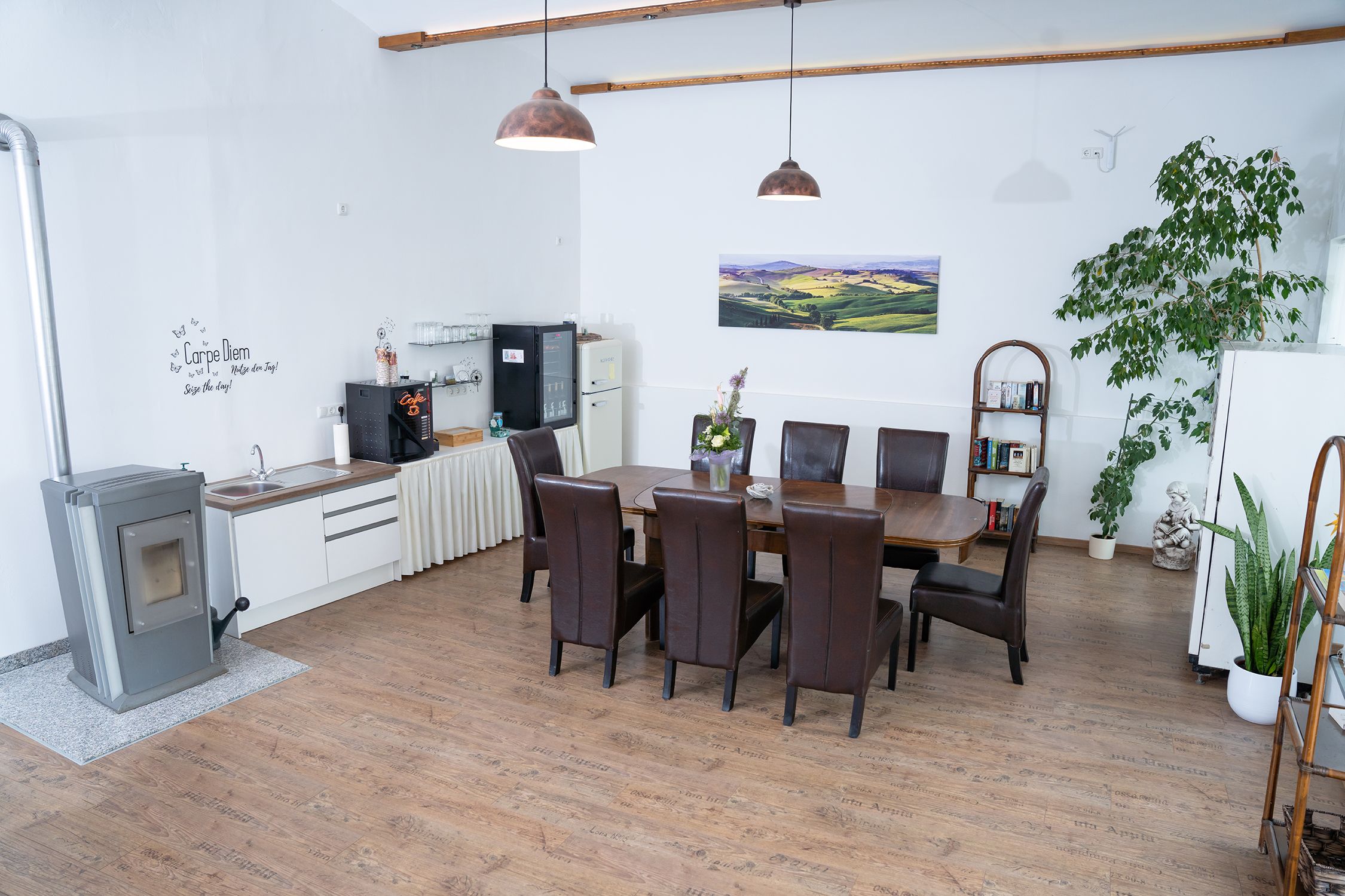 Hangulatos szoba étkezőasztallal, székekkel, növényekkel és konyhasarokkal.