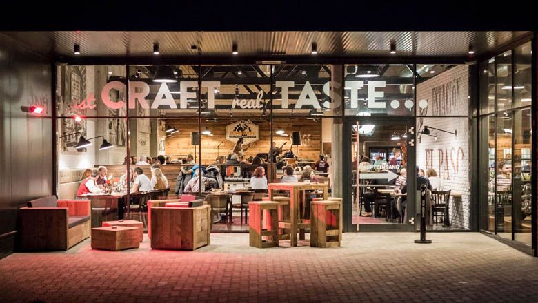 Egy étterem külső nézete, üvegfronttal és fabútorokkal.