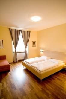 Hangulatos kétágyas szoba nagy ággyal, fapadlóval, fotelrel és függönyös ablakkal.