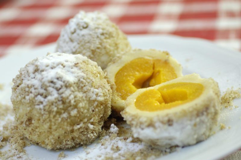 Három sárgabarackos gombóc egy tányéron, az egyik szeletelve.