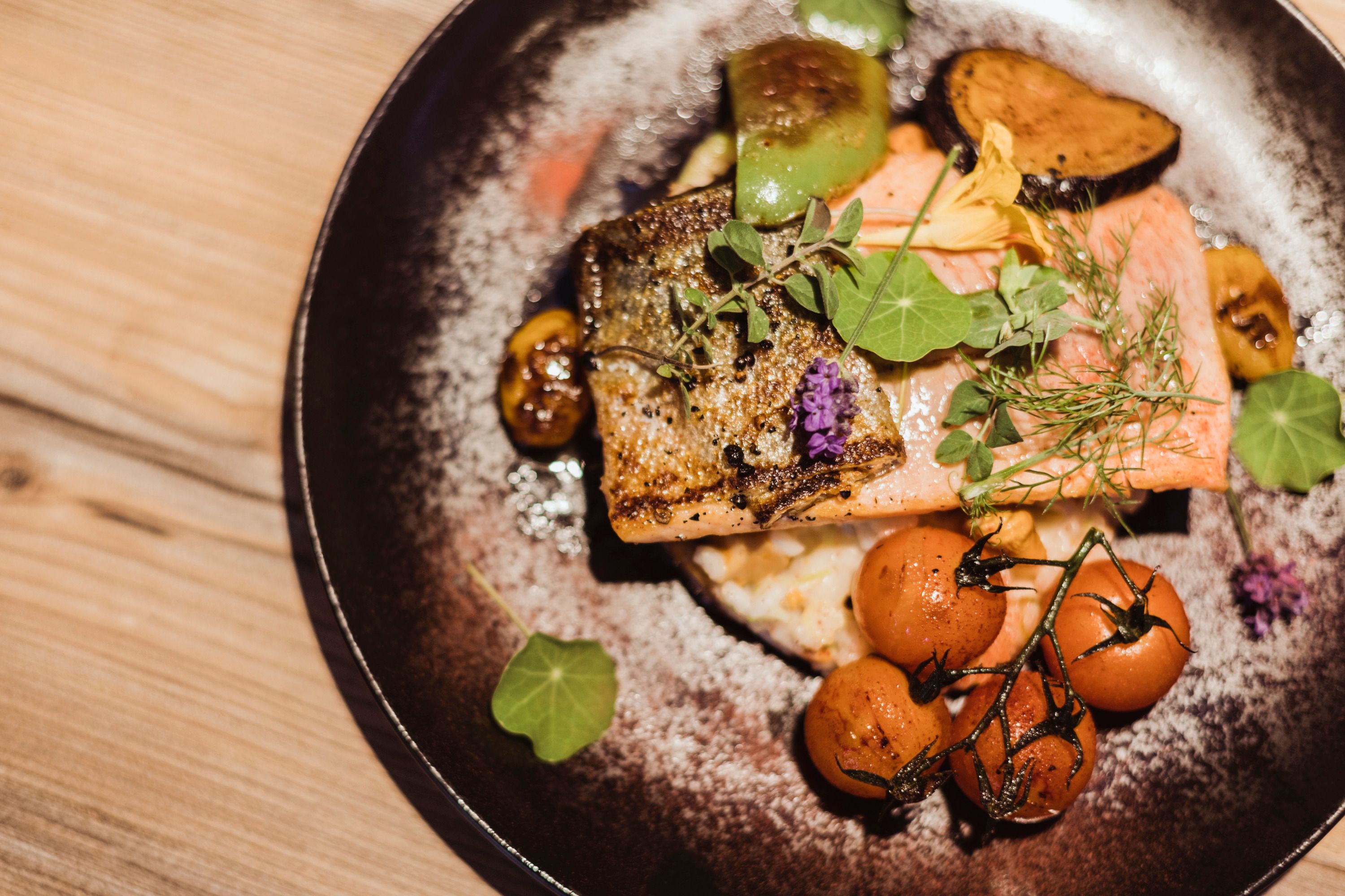 Lazacpisztrángfilé grammel rizottó tányéron zöldségekkel és fűszernövényekkel.