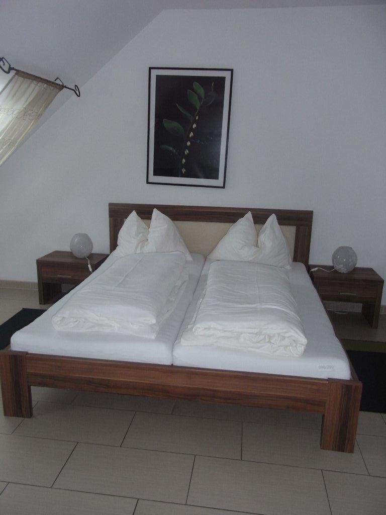 Franciaágy egy szállodai szobában, fehér ágyneművel és egy növényképpel a falon.