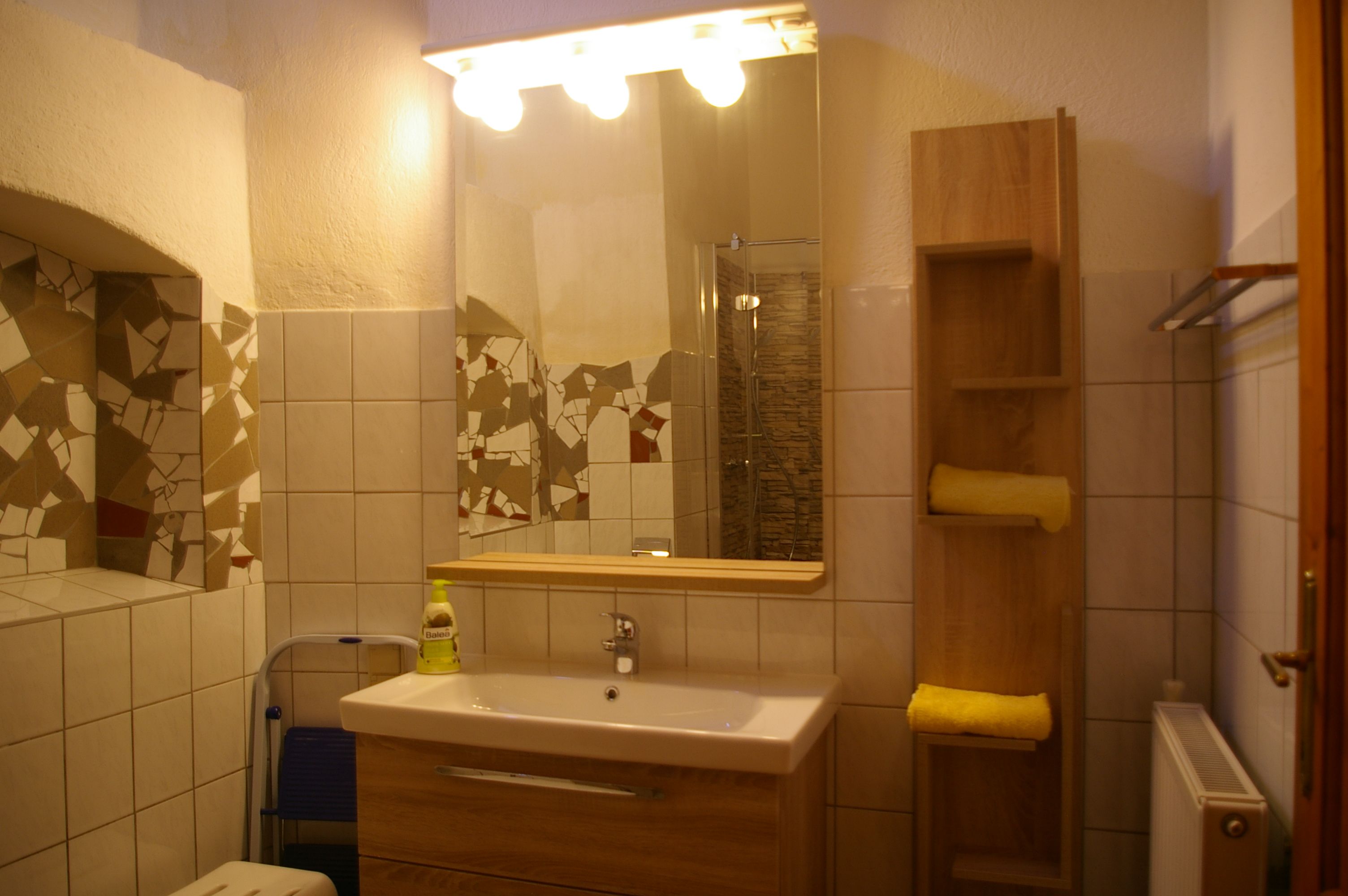 Fürdőszoba tükörrel, mosdókagylóval, csempével és törölközős polccal.